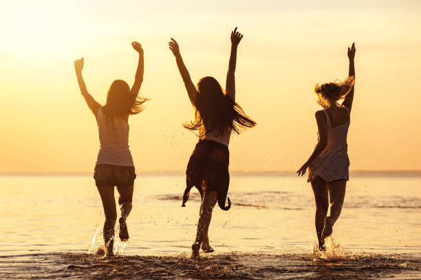Three happy girls at calm sea beach and sunset stock photo