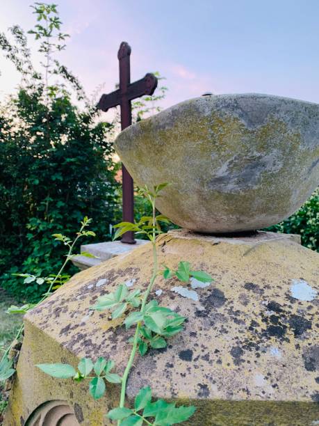 istock Old weathered stone bowl on gravestone, crucifix in background 1182672135