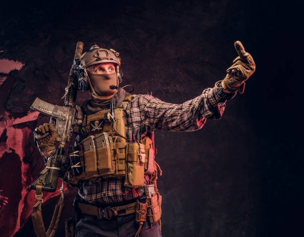 istock Special forces soldier in camouflage uniform posing with assault rifle, looks sideways and shows the middle finger. 1182674042