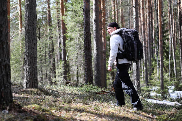 istock A man is a tourist in a pine forest with a backpack. A hiking trip through the forest. Pine reserve for tourist walks. A young man a hike in the spring. 1182680877