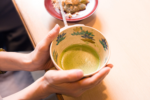 Cup of fresh green matcha tea and bamboo whisk on light grey table, closeup
