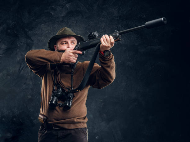 istock Hunter holding a rifle and aiming at his target or prey. Studio photo against dark wall background 1182682483