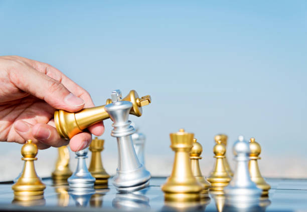 istock Man hand moving golden king in chess game 1182684438