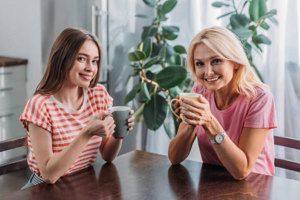 istock happy mother and daughter smiling at camera while sitting at kitchen table with tea cups 1182687457