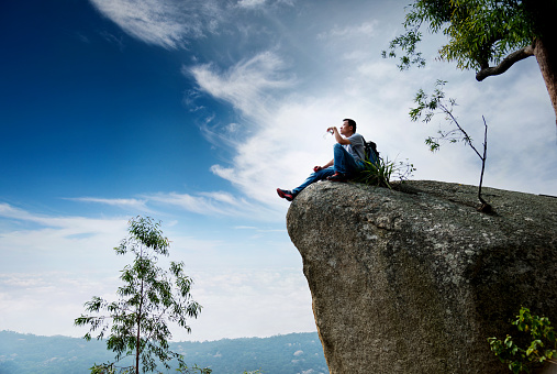 Hiking man sitting on the rock drinking water.