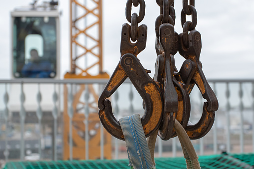 Closeup of four crane hooks with straps attached with crane operator in the background