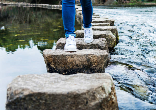 femme traversant des pierres de marche sur une rivière - stepping stone stone stepping footpath photos et images de collection