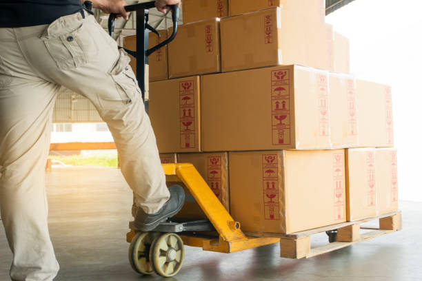 istock Worker working with hand pallet truck unloading package boxes at warehouse 1182696552