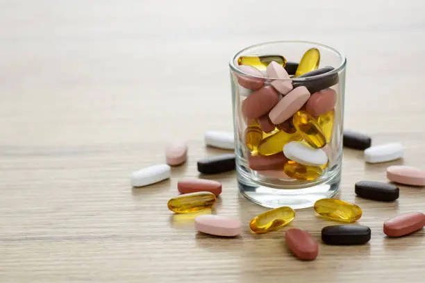 Fish oil capsules and Multivitamin supplements in the small glass on the wooden table with copy space.