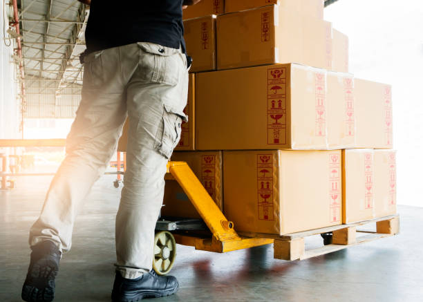 istock Worker working with hand pallet truck unloading package boxes at warehouse 1182696753