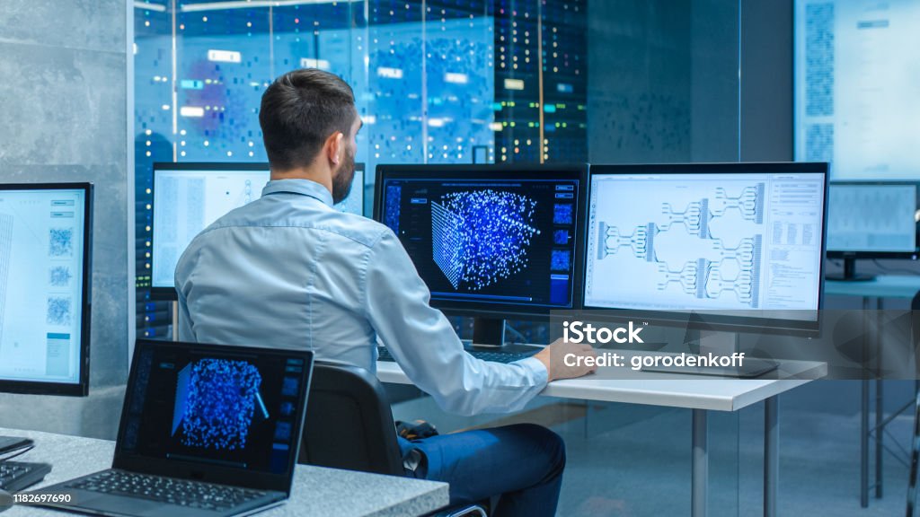 Beautiful Male Computer Engineer and Scientists Create Neural Network at His Workstation. Office is Full of Displays Showing 3D Representations of Neural Networks. Data Stock Photo