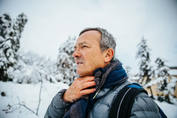 senior man outdoors, holding his neck, experiencing throat pain