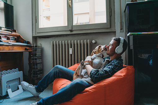 Young adult man listening to music in his bedroom with his dog
