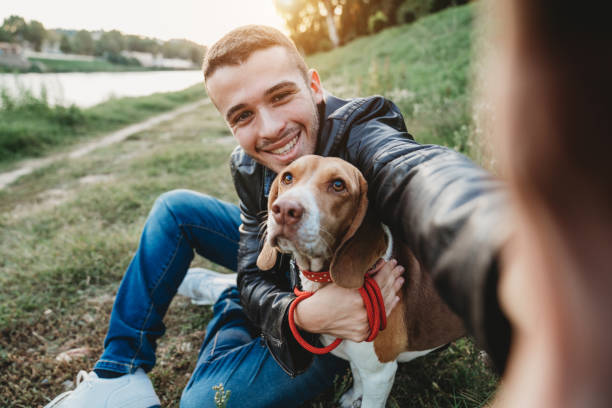市内の川の近くで彼の犬と自分撮りを取る若い大人の男 - pets embracing one person portrait ストックフォトと画像