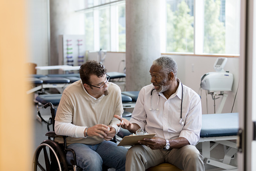 The mid adult wheelchair bound patient listens carefully as the mature adult male doctor explains the treatment plan.