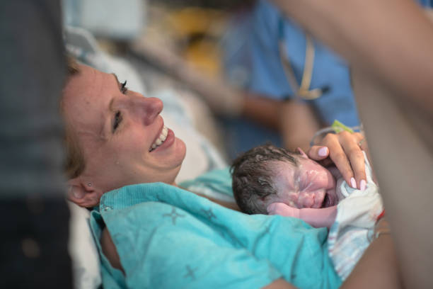 A Mother Holding her Newborn Baby in the Delivery Room for the First Time stock photo A Mother smiles as she holder her newly born infant for the very first time on her chest labor childbirth photos stock pictures, royalty-free photos & images