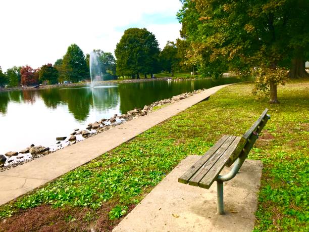 istock Park bench with fountain green grass and trees in the fall 1182714060