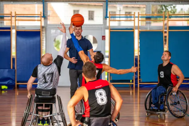 Two basketball players in wheelchairs struggling for the ball during a tip-off in a gymnasium.