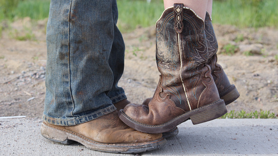 Couple standing together.  Country girl standing on tiptoes on her man's boots.