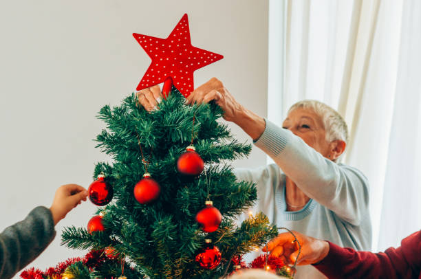 Senior woman decorating the Christmas tree Beautiful senior woman putting the Christmas star on top of the Christmas tree. tree topper stock pictures, royalty-free photos & images