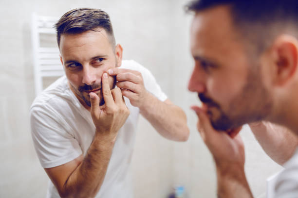 close up of handsome caucasian man looking himself in the mirror and squeezing blackhead on his cheek. - shirt lifestyles close up cheerful imagens e fotografias de stock