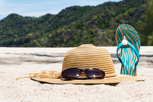 Straw hat, sunglasses and flip flops on a tropical beach. Summer vacation concept.