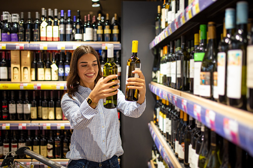 Woman with bottles of rose and white wine in store. Woman deciding what wine to buy. Woman holding bottles of wine in supermarket. Woman choosing a wine, champagne at supermarket