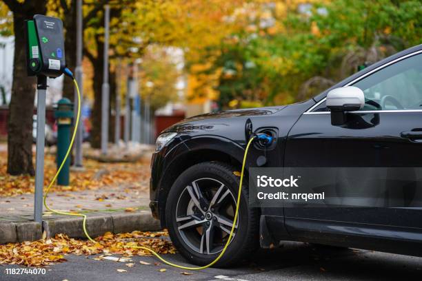 Volvo Car Is Plugged In For Charging On Street Parking Lot With Beautiful Autumn View Background Stock Photo - Download Image Now
