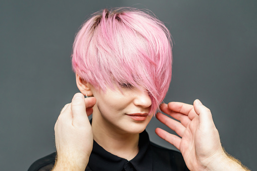 Hands of hairdresser is checking short pink hair of girl on gray background close up. Hairdresser checks short pink hairstyle of young woman.