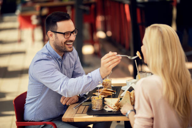 Happy couple sharing food and having fun during lunch in a restaurant. Happy couple eating in a restaurant. Man sharing his food and feeding his girlfriend. sandwich club sandwich lunch restaurant stock pictures, royalty-free photos & images
