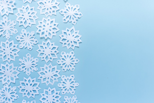Arrangement of many white handmade paper snowflakes on blue background. Photo with blank space for greeting text.