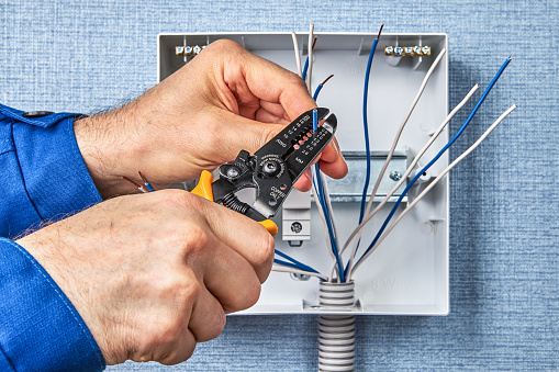 Installing of automatic fuses on a DIN rail. DIY wiring a consumer unit or  distribution board installation. Stripping the end of the copper wire with the stripper cutting tool.