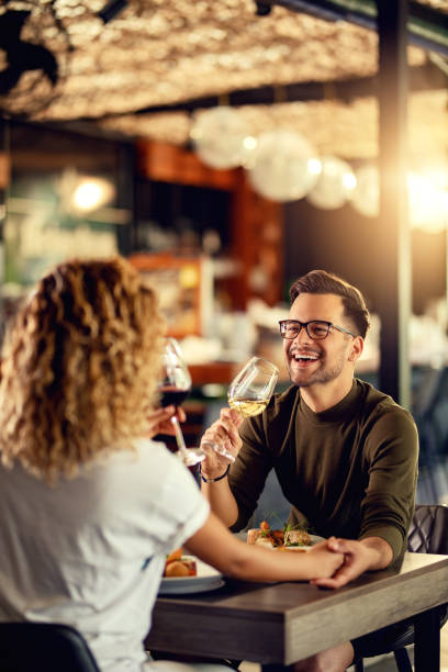 Cheerful man having fun while drinking wine with his girlfriend in a restaurant. Young couple drinking wine and having fun during lunch in a bar. Focus is on man. dining stock pictures, royalty-free photos & images