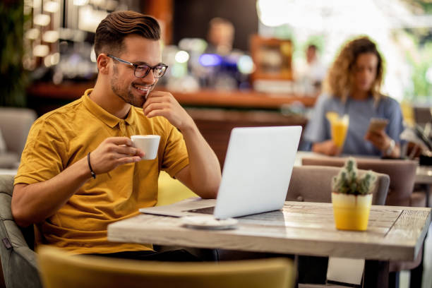 istock Smiling man reading an e-mail on laptop and drinking coffee in a bar. 1182754322