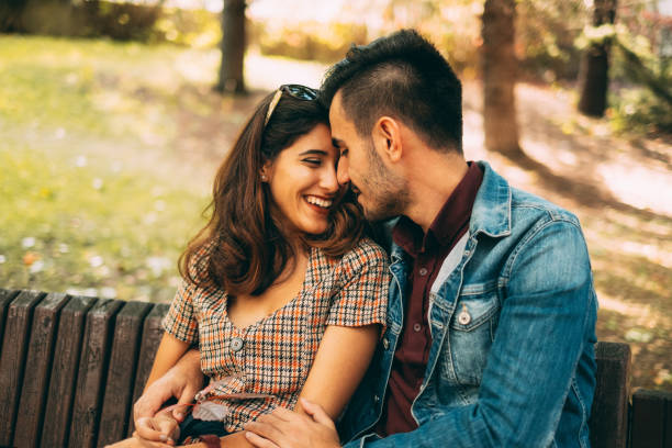 istock Young Couple Sitting on Bench in Park 1182758534