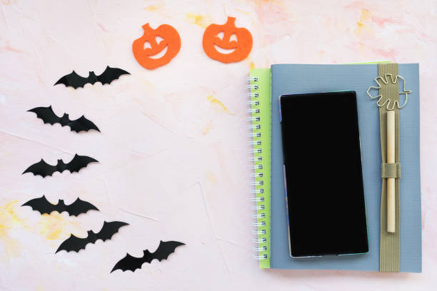 istock Notebook, pen, pumpkin, bats and a phone background. Halloween concept. 1182758908