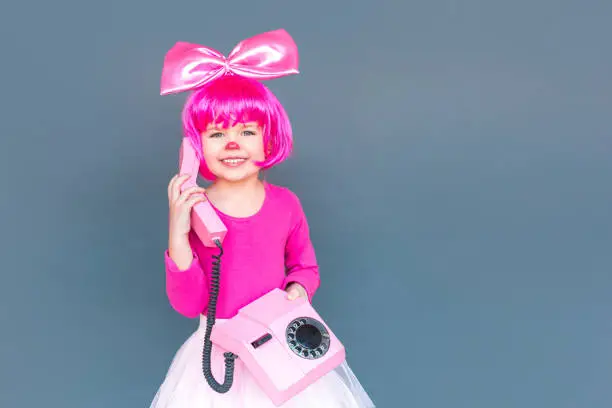 Photo of Portrait of little clown girl calling on old pink phone