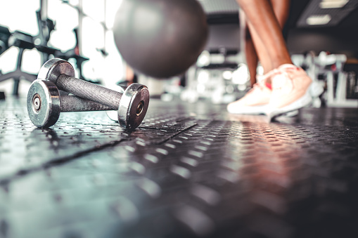 Dumbbell on a flor in fitness gym with black woman legs on background.