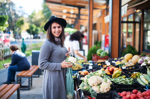 Young woman buying fruit and vegetables at outside market, she holding cauliflower and looking at camera.