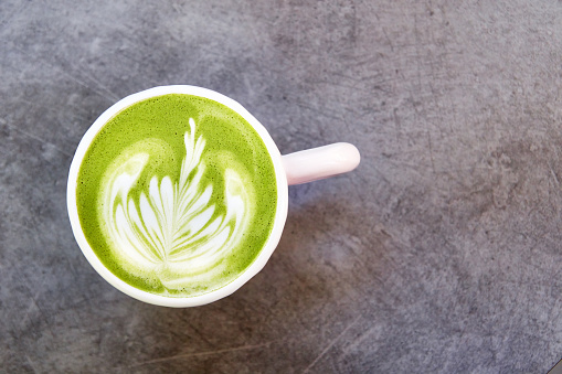 Vegan green tea matcha with oat milk with latte art in white cup on concrete table. Top view, with place for text.