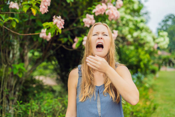 Young woman sneezes in the park against the background of a flowering tree. Allergy to pollen concept Young woman sneezes in the park against the background of a flowering tree. Allergy to pollen concept. hayfever stock pictures, royalty-free photos & images
