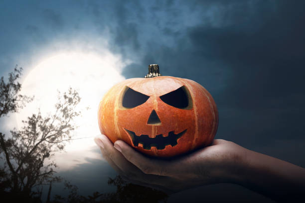 istock Hand holding Jack-o-lantern with a full moon 1182776273