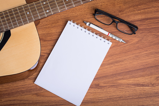 guitar notebook, pencil and eyeglasses on wooden background