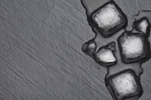 Melting ice cubes on the dark black slate background with copy space