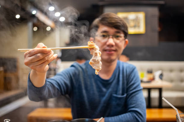 uomo che tiene le bacchette che mangiano carne - buffet thai cuisine asian ethnicity food foto e immagini stock
