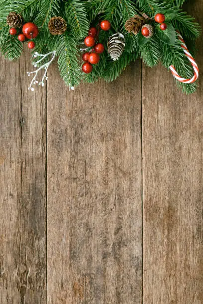 Photo of Wood table plank in vertical with pine leaves and pine cones, holly balls and candy cane in Christmas theme concept. Wooden background in top view flat lay with copy space for Christmas wallpaper.