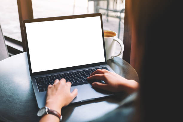 a woamn using and typing on laptop with blank white desktop screen with coffee cup on the table