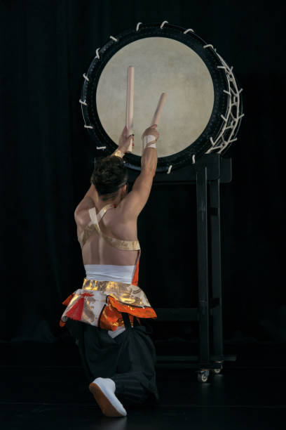 el baterista de taiko golpea el tambor grande en el escenario en un fondo negro, vista posterior. - taiko drum fotografías e imágenes de stock