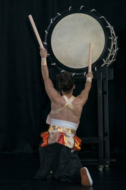 istock Taiko drummer hits the big drum on stage on a black background, back view. 1182792993