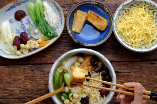 People eating Vietnamese vegan noodle soup for breakfast, vegetarian homemade food from tofu, jujube fruit, lotus seed, bok choy, mushroom, spice